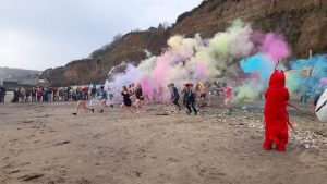 Swimmers run into the sea after throwing colored dye in the air