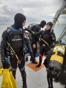 4 divers in black and gold, setting up equipment on the Blue Seas Protection Dive Boat just before Dive for the Great Shark Snapshot Week Survey
